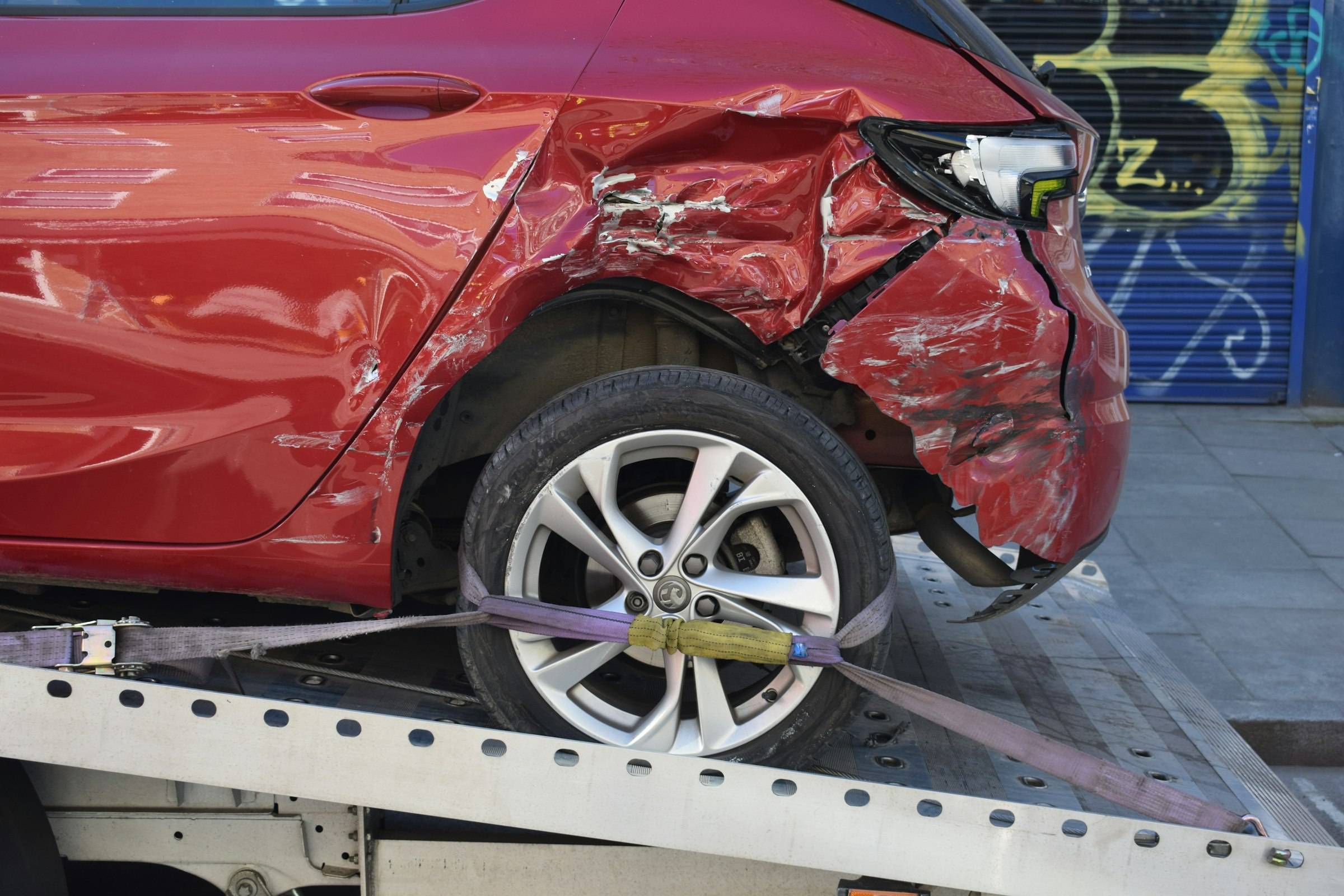 A red car with a crushed rear quarter strapped down on a flatbed deck