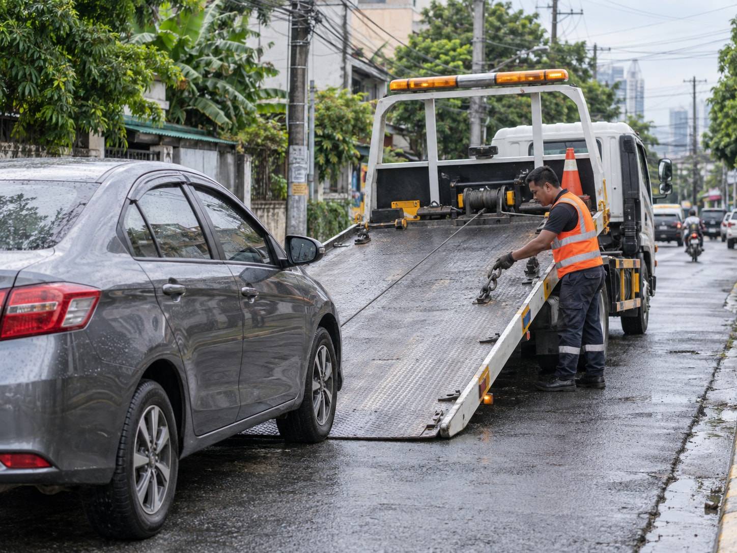 A Filipino tow operator preparing a flatbed to load a sedan on a Metro Manila street