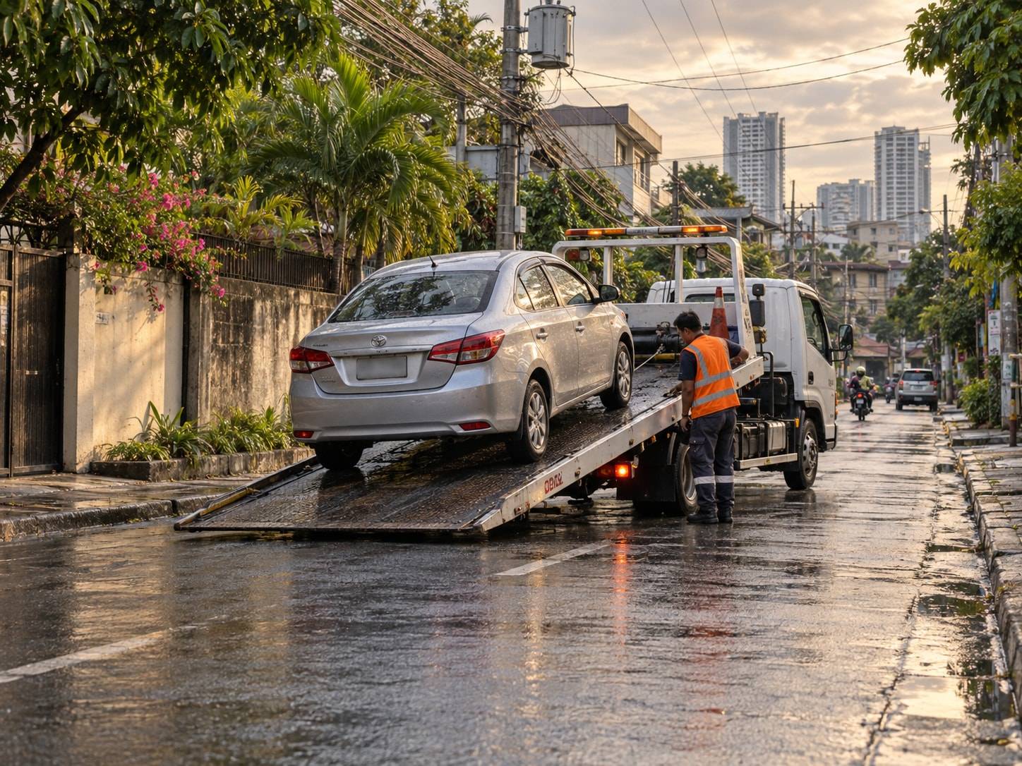 A Filipino tow operator loading a silver sedan onto a flatbed on a Metro Manila street