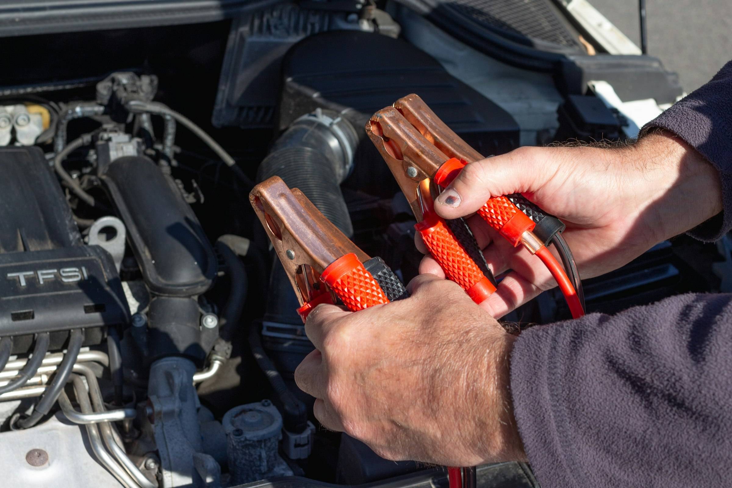 Hands clamping red and black jumper cables inside an engine bay