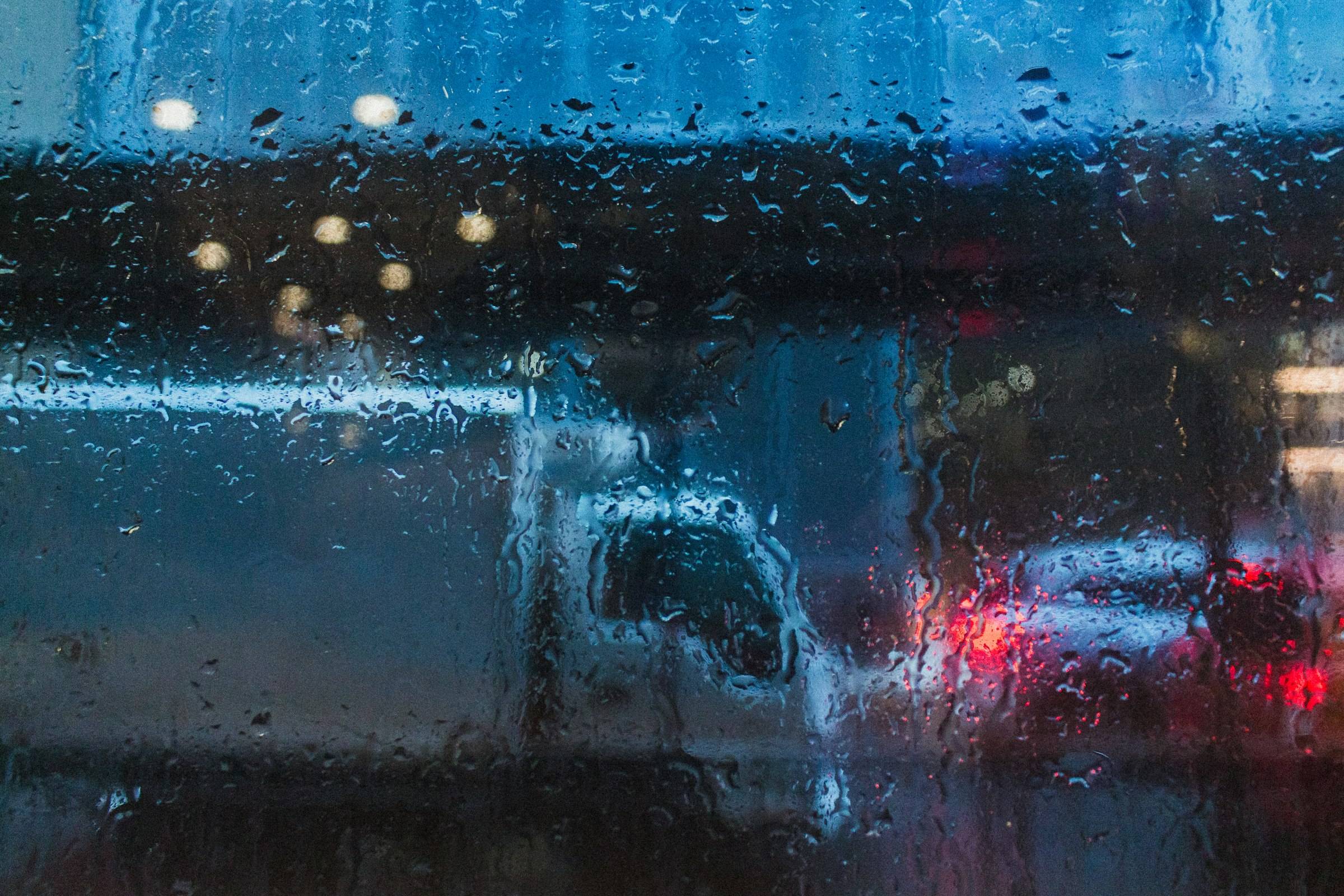 A truck’s tail lights blurred through a rain-streaked window at night