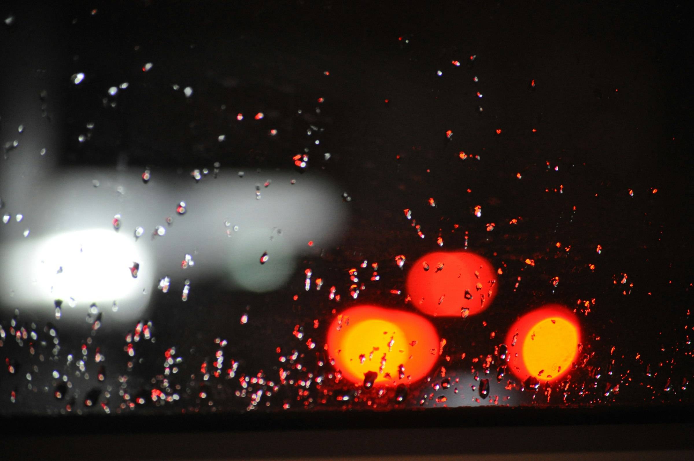 Rain on a windshield at night with red lights blurred beyond it